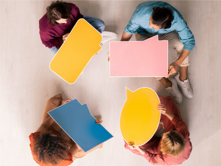 Four people sitting in a circle and holding colored speech bubbles